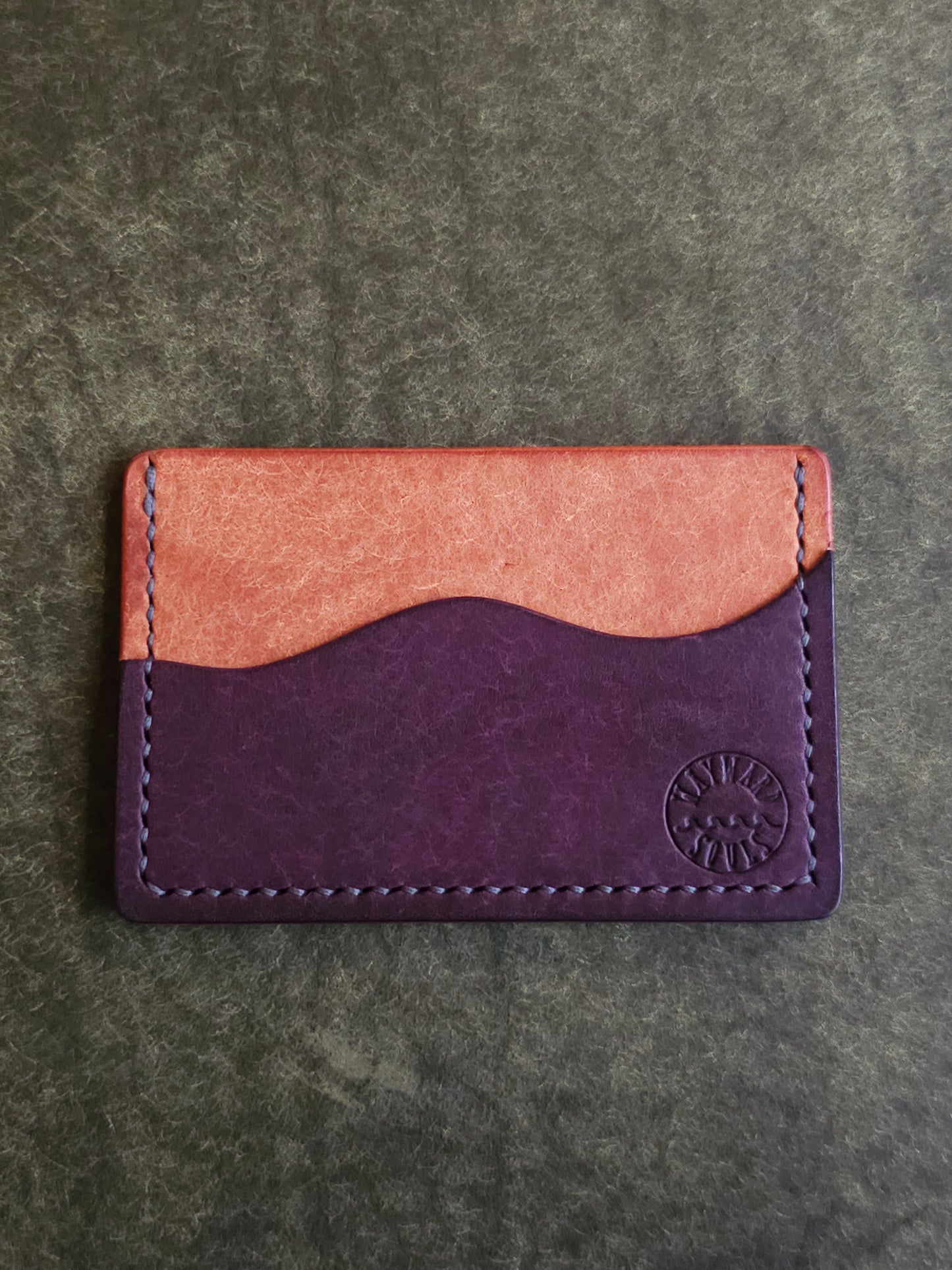 Leather card holder with pocket shaped like a wave. Wayward Souls logo is stamped in the bottom right corner of the wallet.