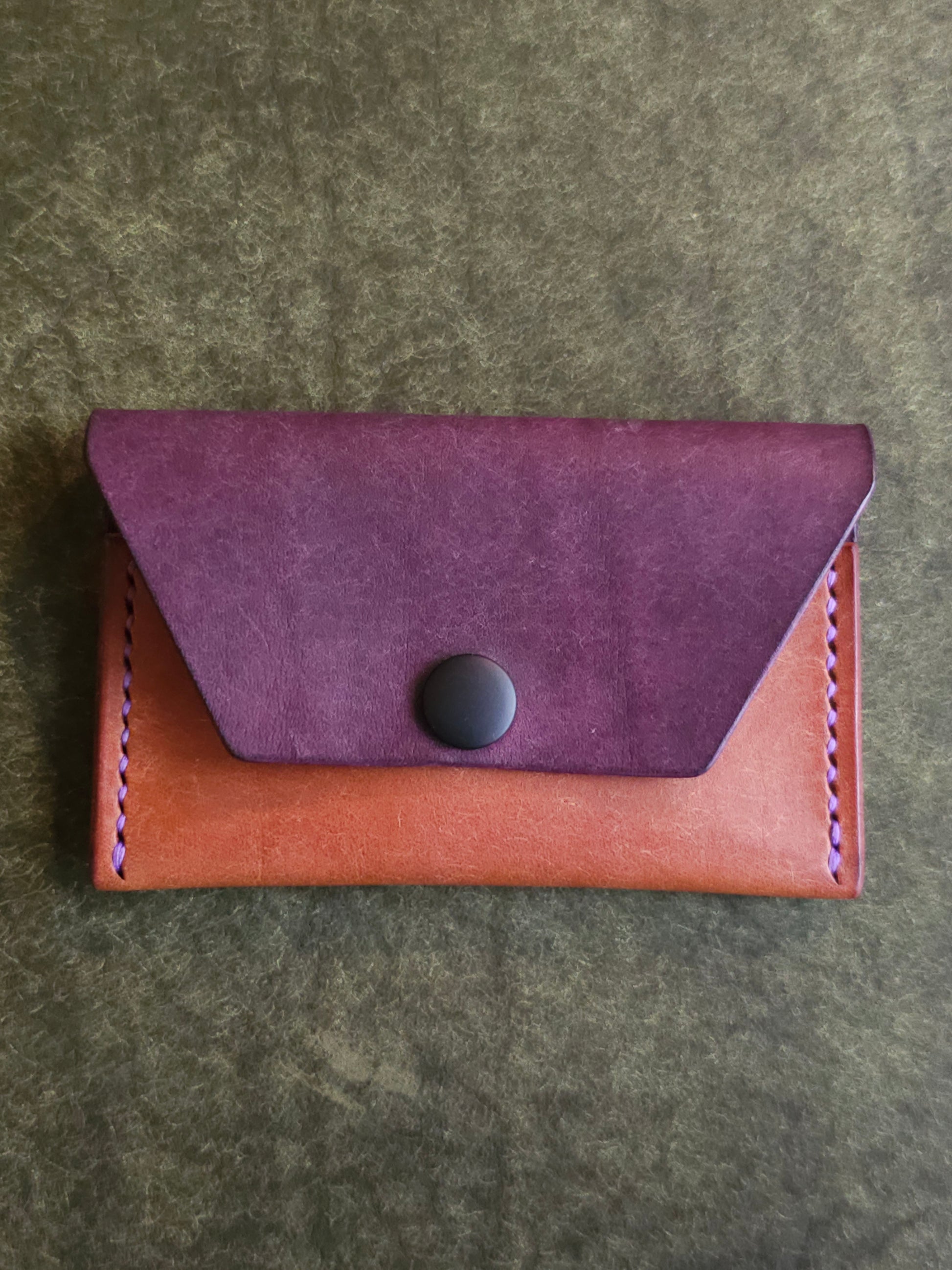 Front of leather card holder with angled pocket fastened with a snap.
