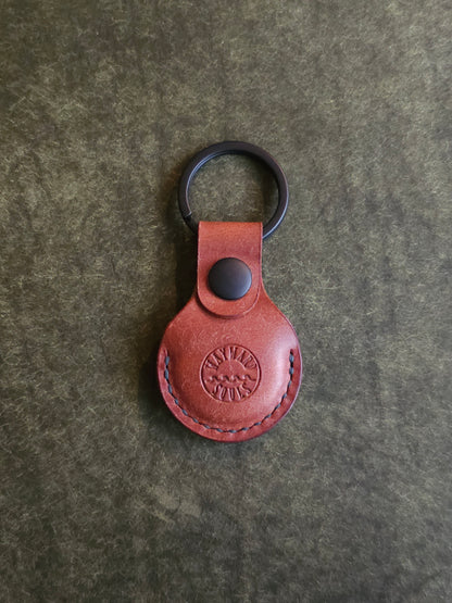 Circular leather air tag holder attached to black key ring. The Wayward Souls logo is stamped into the center.