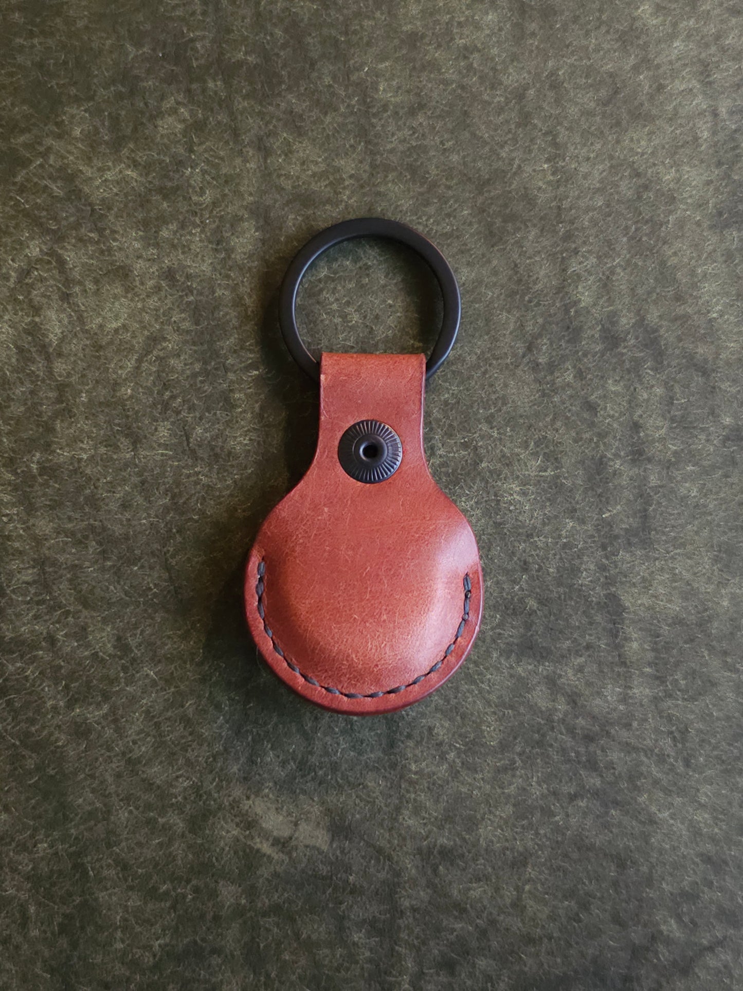 Back of circular leather air tag holder attached to black key ring. 