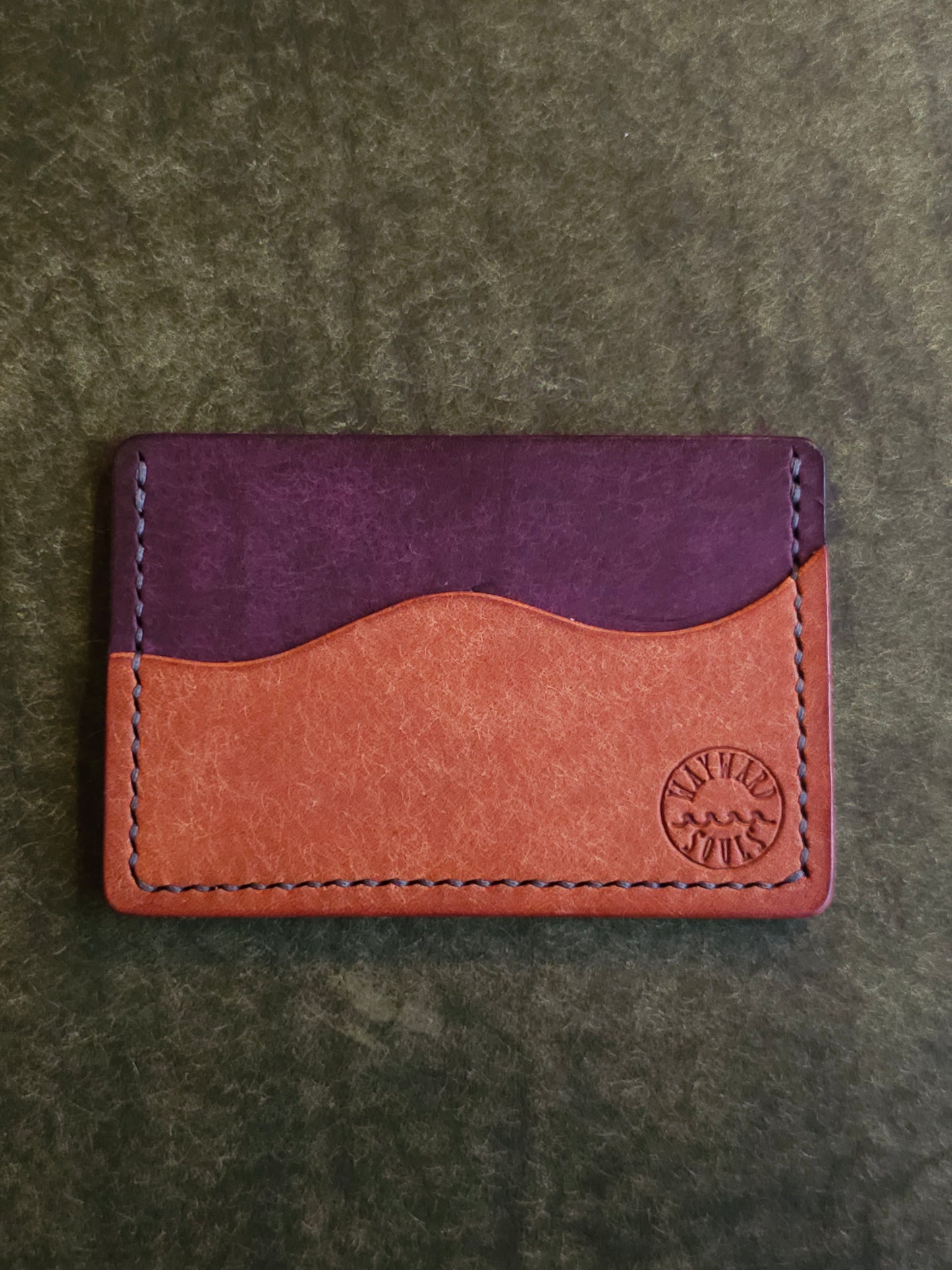 Leather card holder with pocket shaped like a wave. Wayward Souls logo is stamped in the bottom right corner of the wallet.