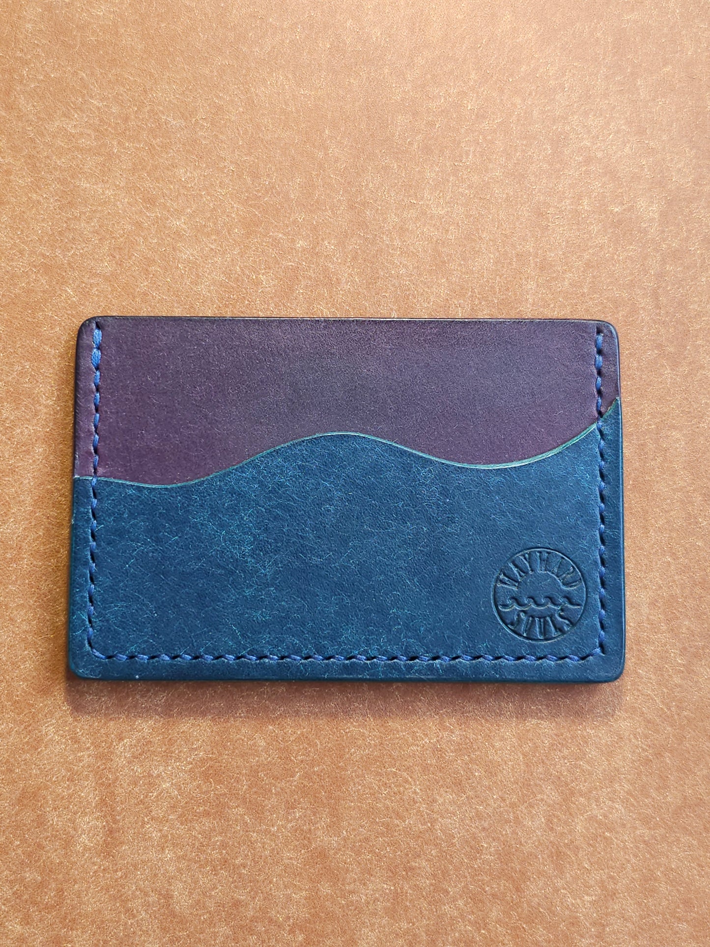 Leather card holder with pocket shaped like a wave. Wayward Souls logo is stamped in the bottom right corner of the wallet.