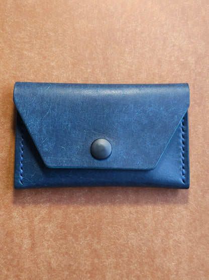 Front of leather card holder with angled pocket fastened with a snap.