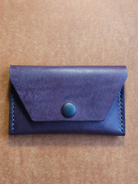 Front of leather card holder with angled pocket fastened with a snap.