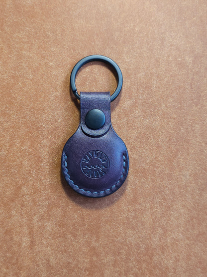 Circular leather air tag holder attached to black key ring. The Wayward Souls logo is stamped into the center.
