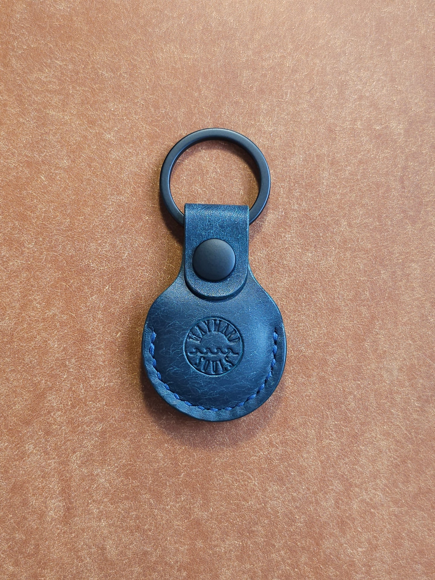 Circular leather air tag holder attached to black key ring. The Wayward Souls logo is stamped into the center.