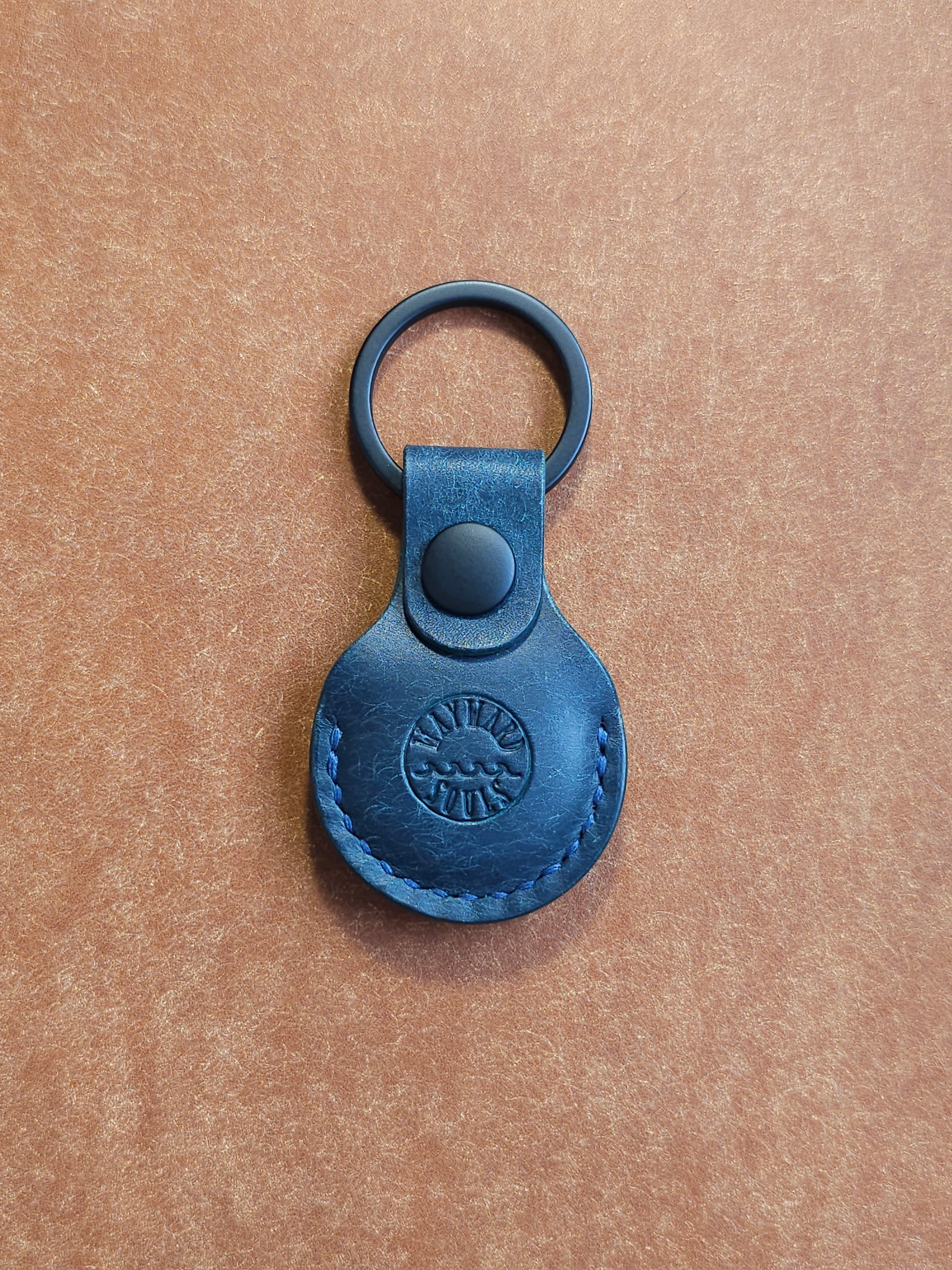 Circular leather air tag holder attached to black key ring. The Wayward Souls logo is stamped into the center.