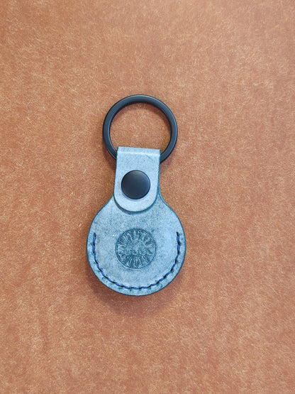 Circular leather air tag holder attached to black key ring. The Wayward Souls logo is stamped into the center.