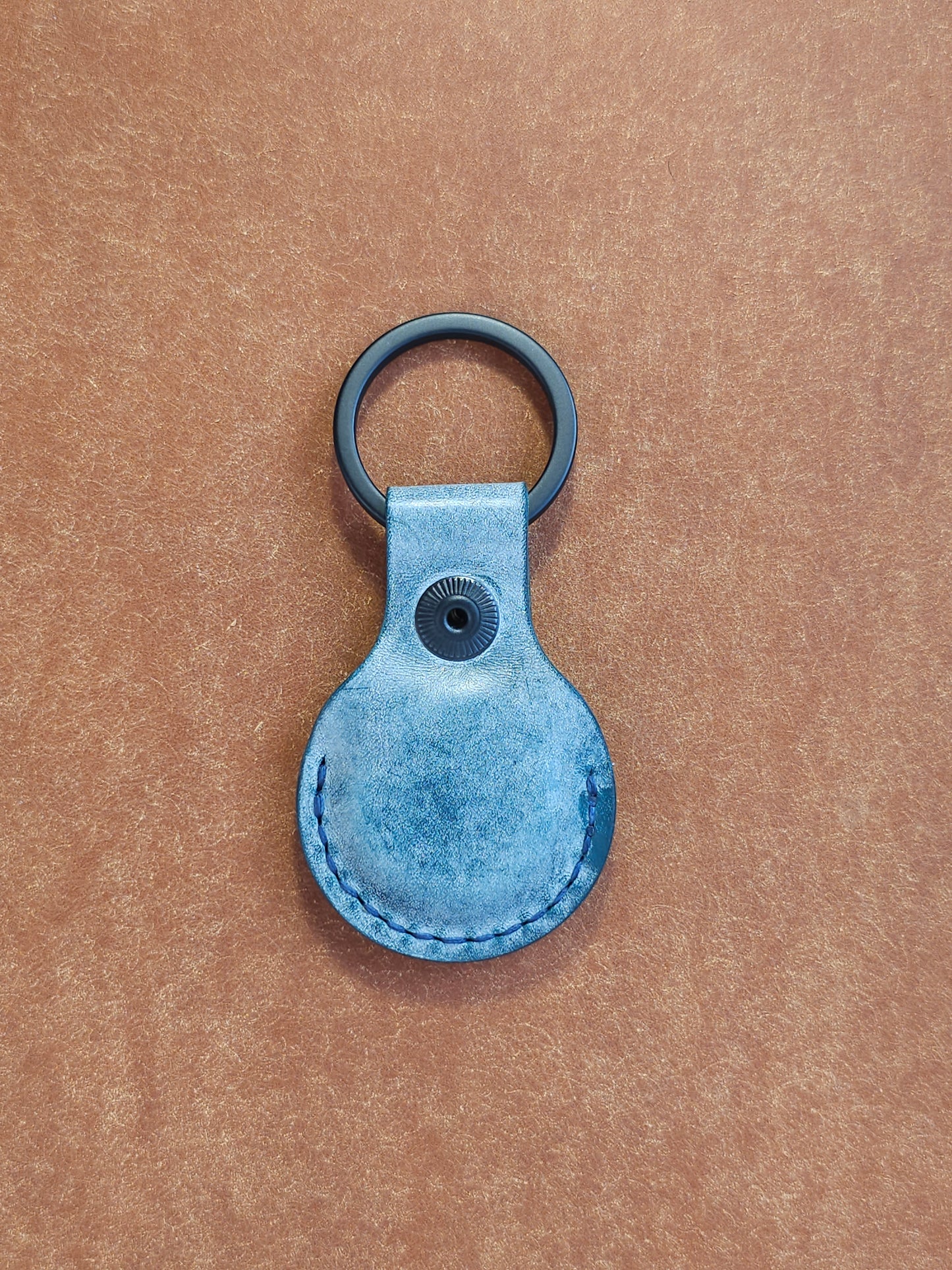 Back of circular leather air tag holder attached to black key ring.