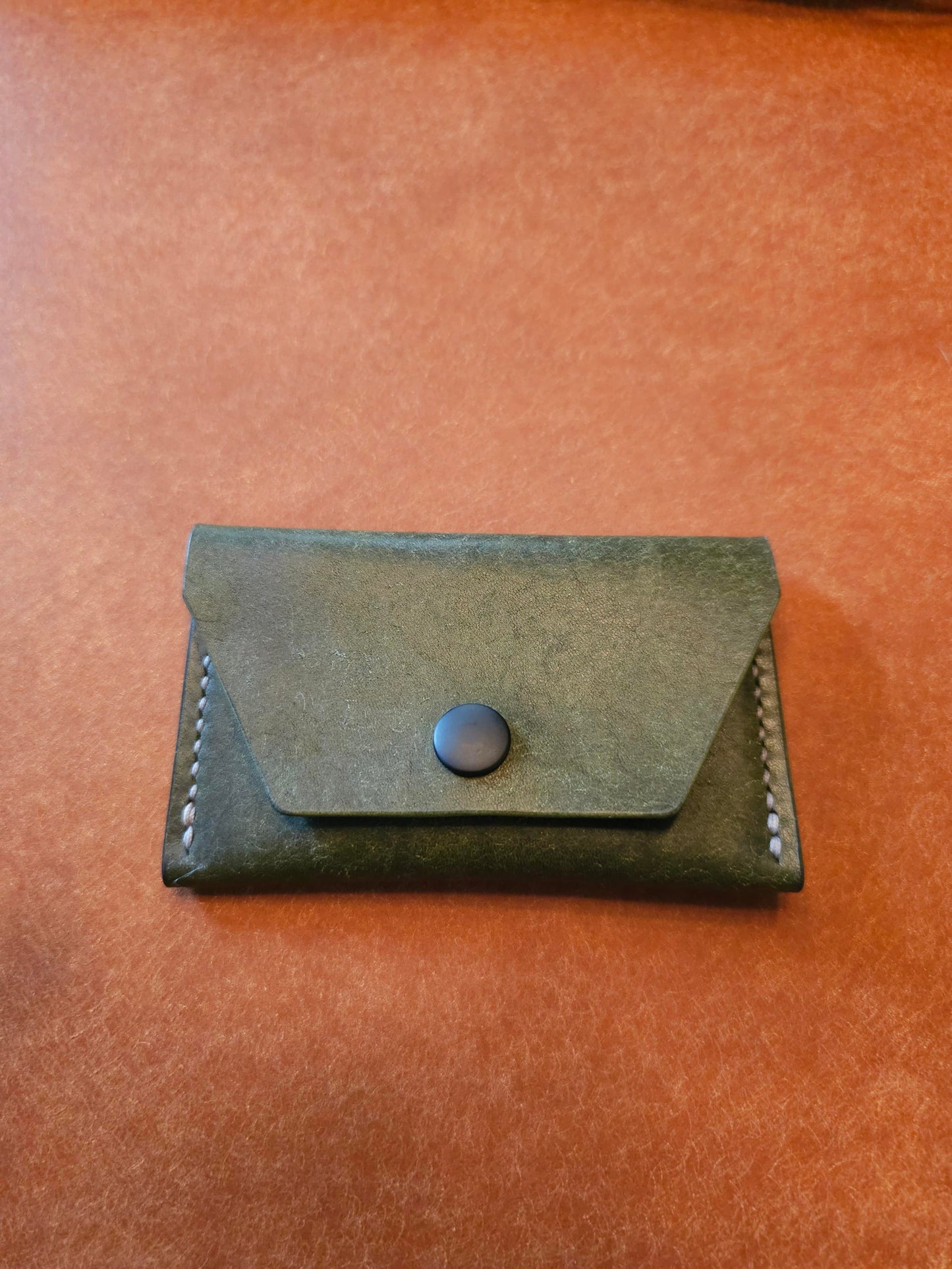 Front of leather card holder with angled pocket fastened with a snap.