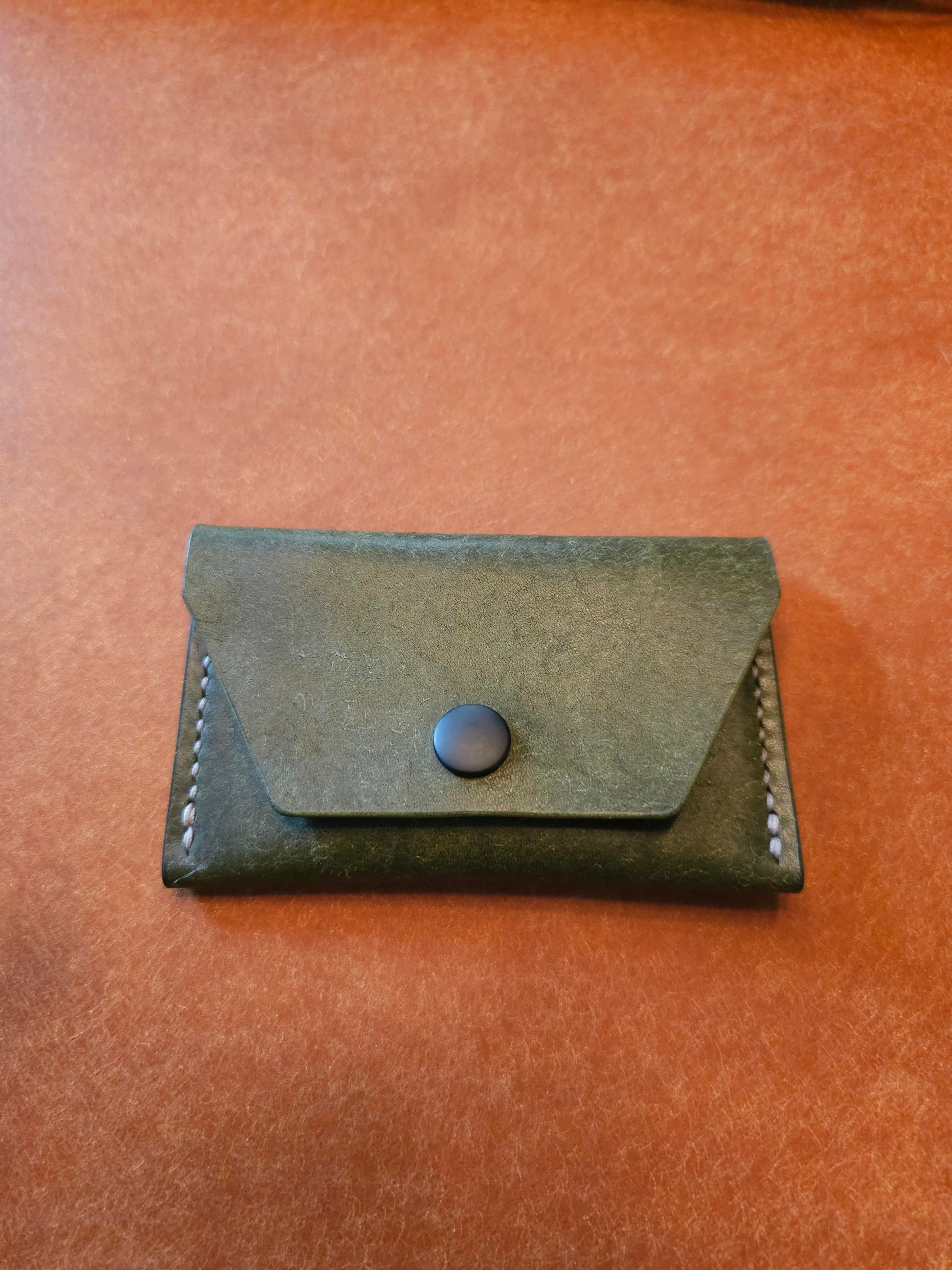 Front of leather card holder with angled pocket fastened with a snap.